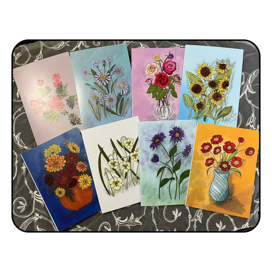 Flat lay of eight floral art note cards from Tora Moon’s Blooming Expressions set, showing all designs—sunflowers, asters, roses, fortnight lily, red cosmos, bottle brush, pumpkin bouquet, and purple daisies—arranged on a floral background.