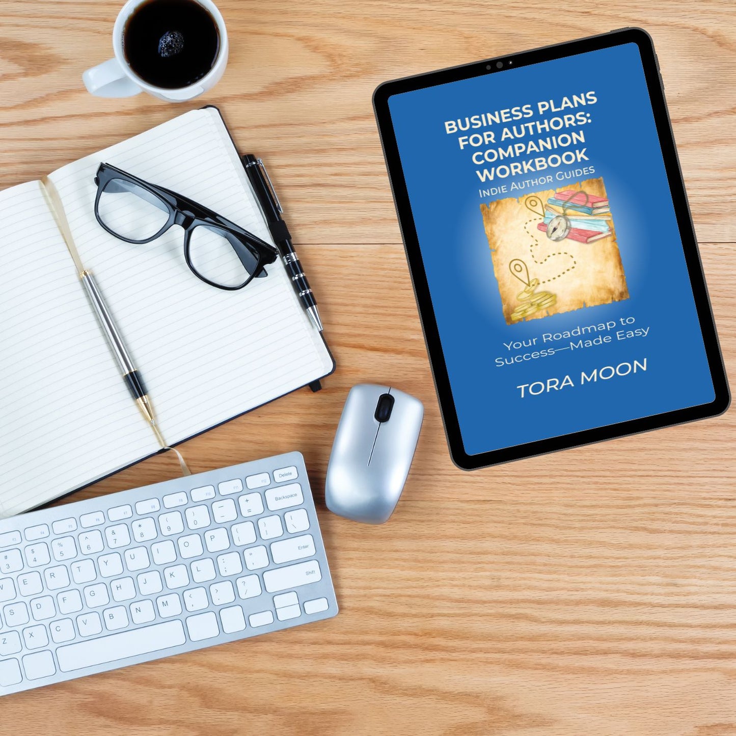 Lifestyle image of the Business Plans for Authors: Companion Workbook displayed on a tablet next to an open notebook, glasses, keyboard, and coffee cup—showcasing a practical, organized workspace for indie authors planning their business.