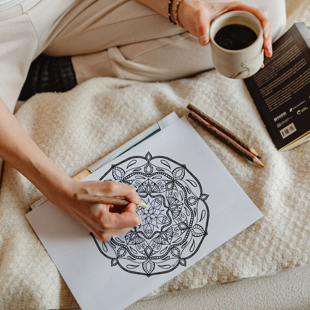 Woman coloring an intricate mandala on a cozy blanket with coffee and journal nearby, representing mindfulness integration practice in Freya's Sacred Worth Guide by Tora Moon.
